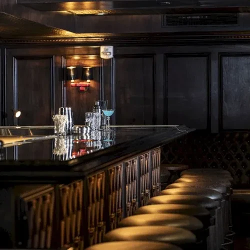 A sophisticated dark bar with stools and cocktail preparation tools.