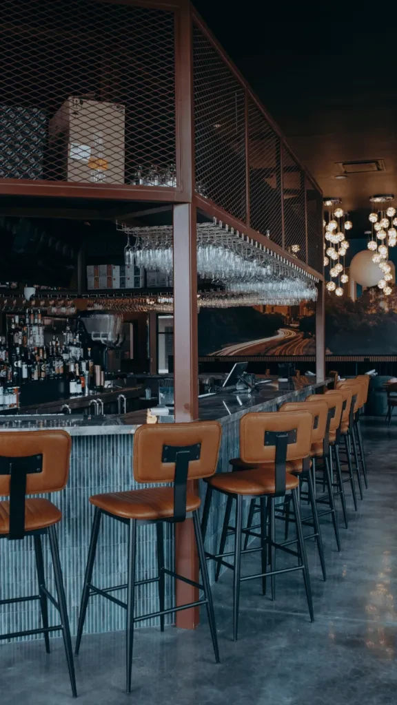 Empty bar with brown leather stools, bottles, and hanging glasses.