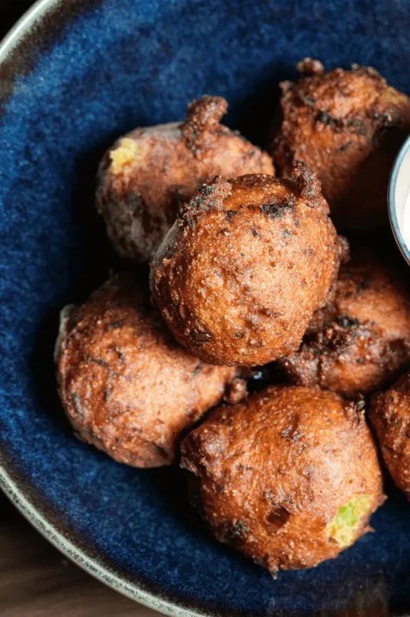 Golden-brown fried fritters or hushpuppies in a dark blue bowl.