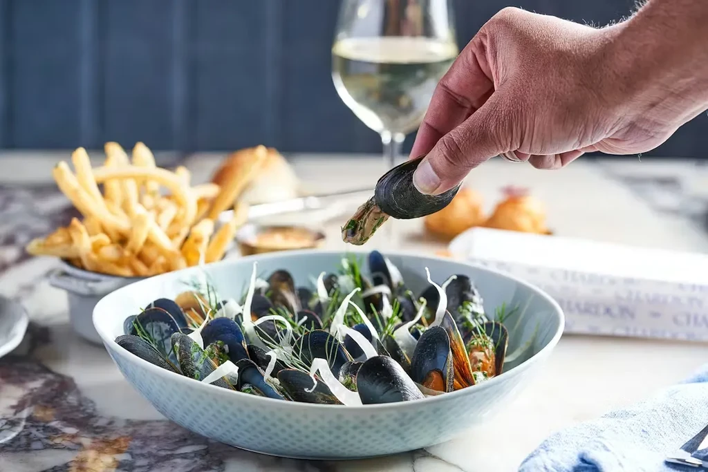 Close-up of a blue bowl of mussels, fries, and white wine.