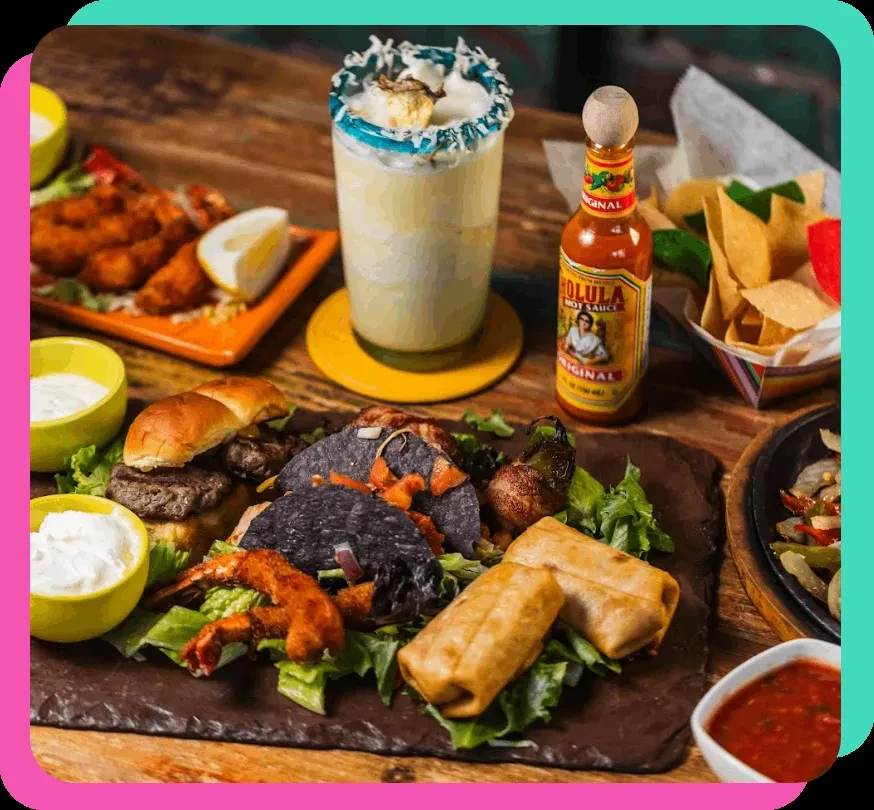 Table with various Mexican food, a drink, Cholula hot sauce, and chips.
