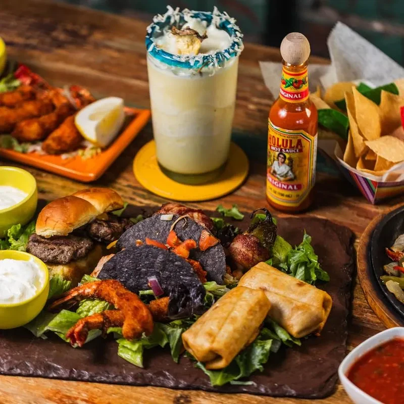 Assortment of Mexican dishes, drinks, and hot sauce on a wooden table.