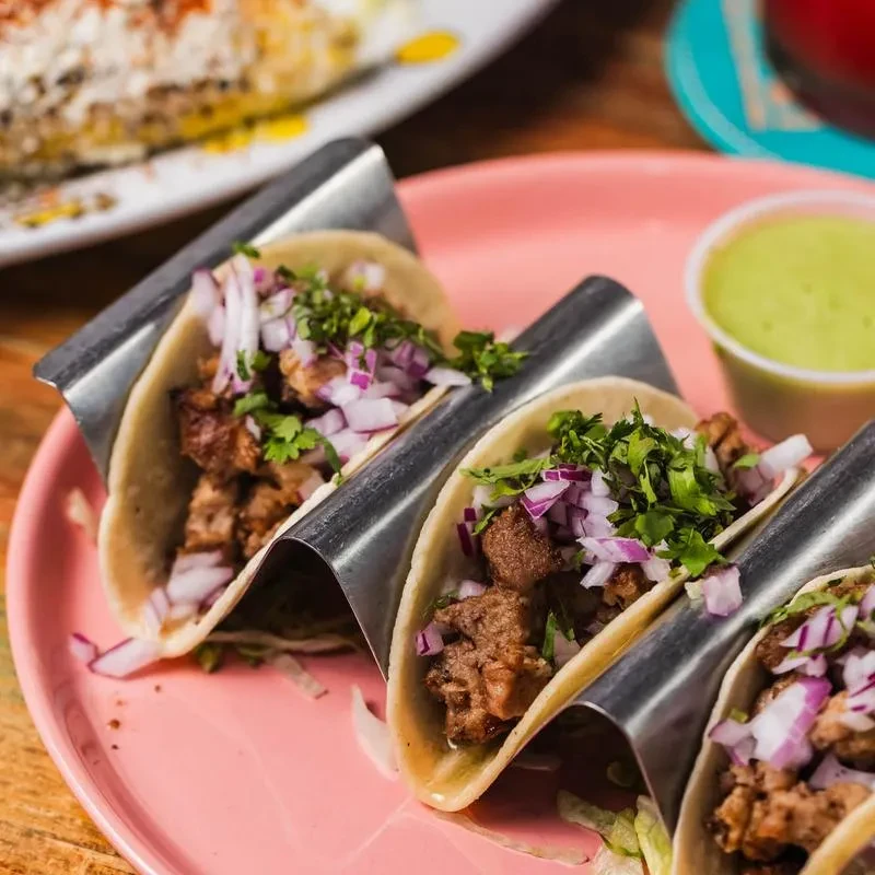 Three street tacos with meat, onions, and cilantro on a pink plate.