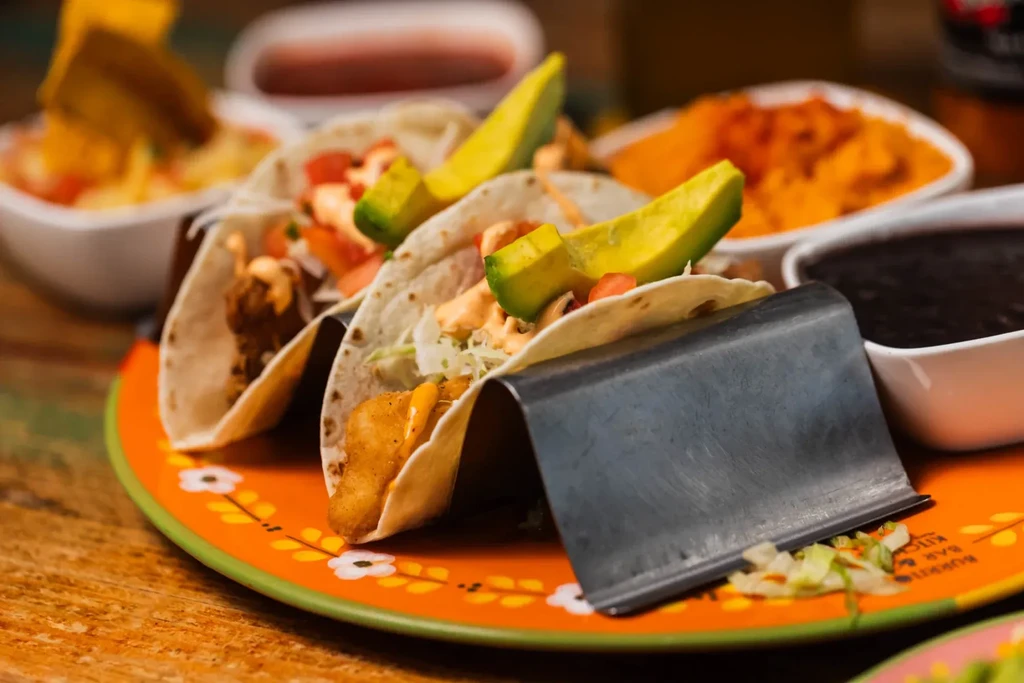 Three tacos in a metal stand on an orange plate.