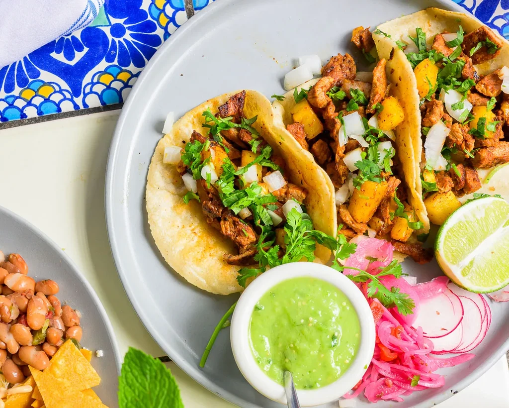Three tacos filled with meat, pineapple, onions, and cilantro on a plate.