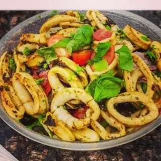 Grilled calamari salad with tomatoes and fresh herbs in a silver bowl.