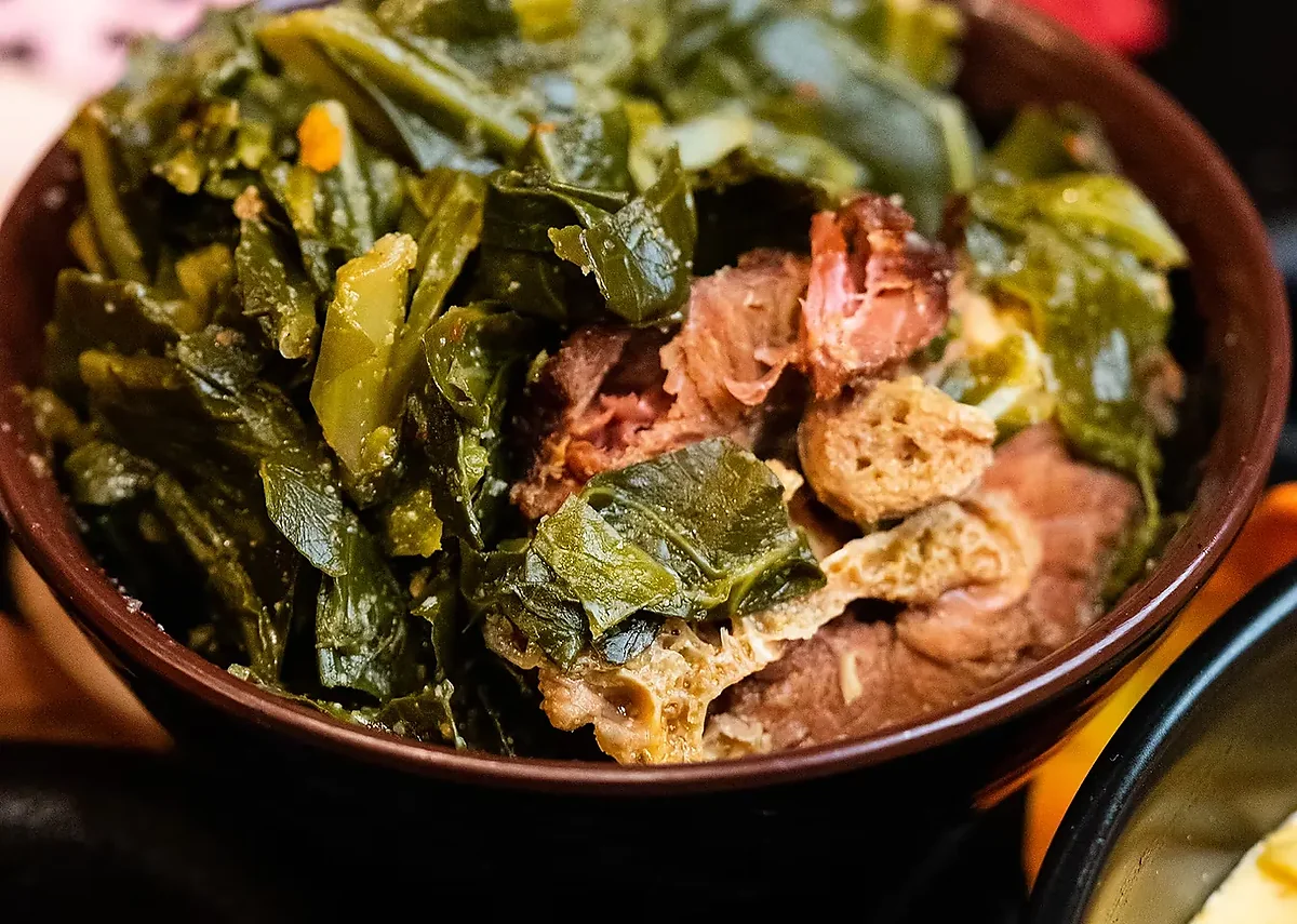 Bowl of braised collard greens with chunks of smoked meat