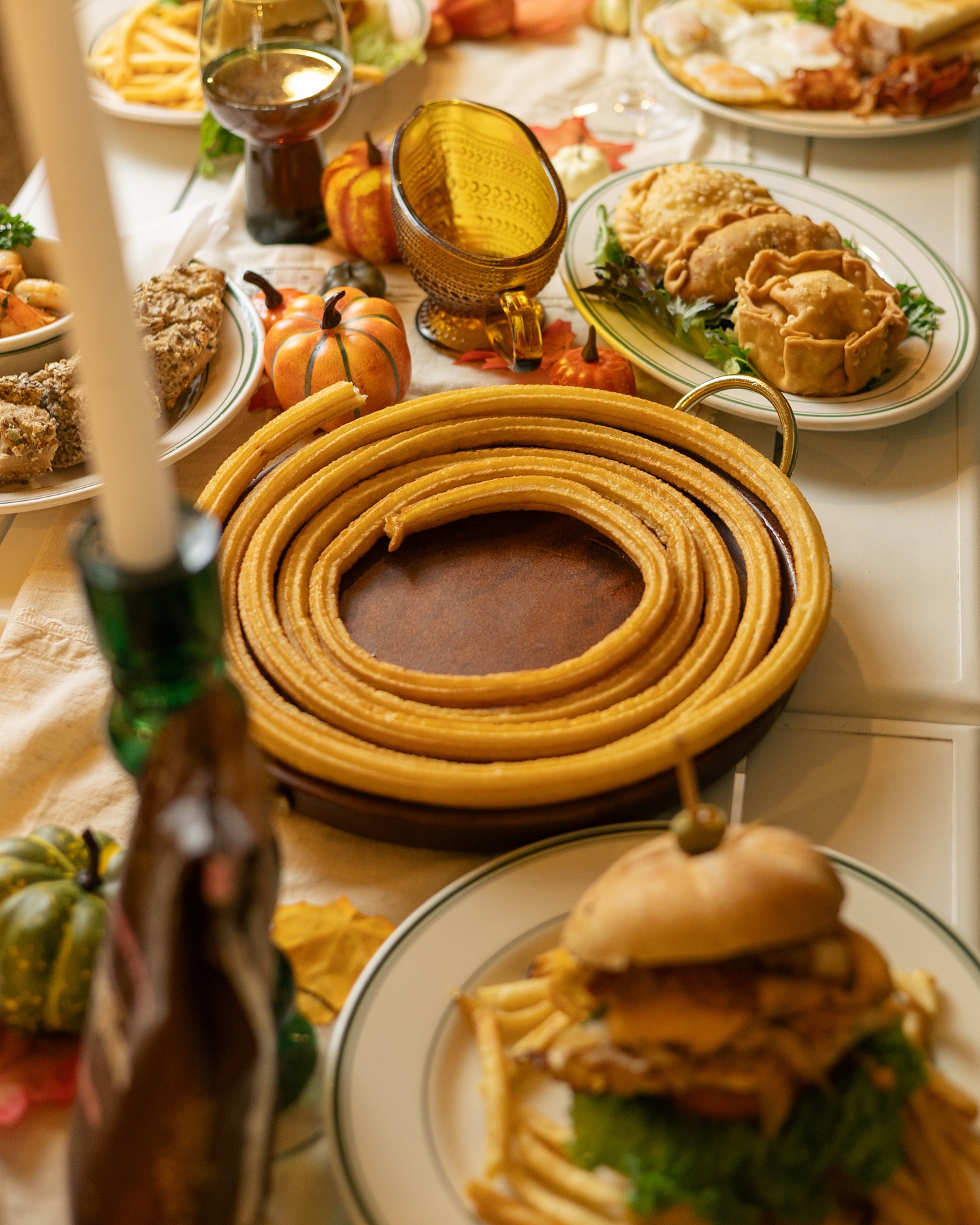 Table laden with coiled churros, empanadas, a burger, and pumpkins.