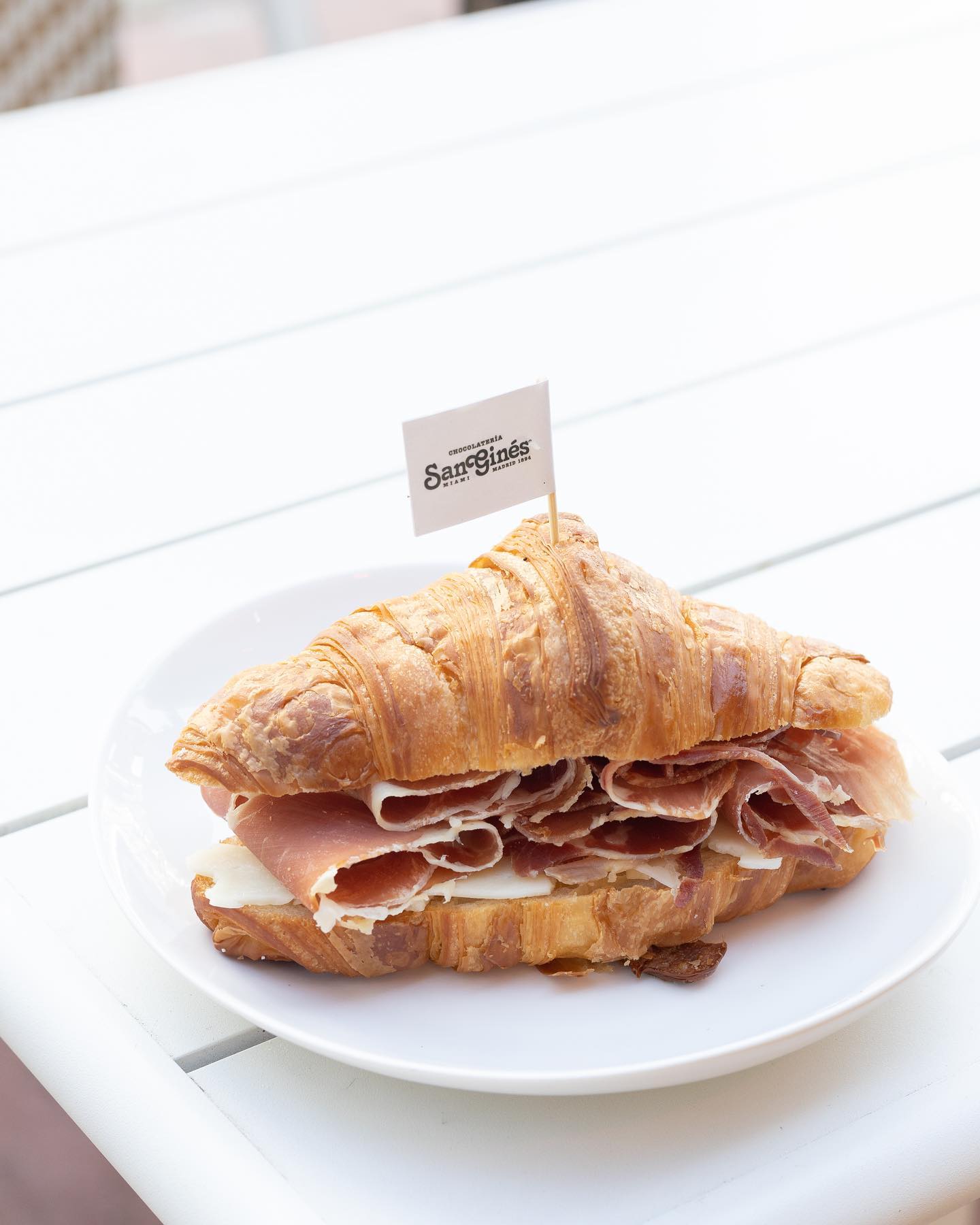 Croissant sandwich with sliced ham, cheese, and a San Ginés flag.