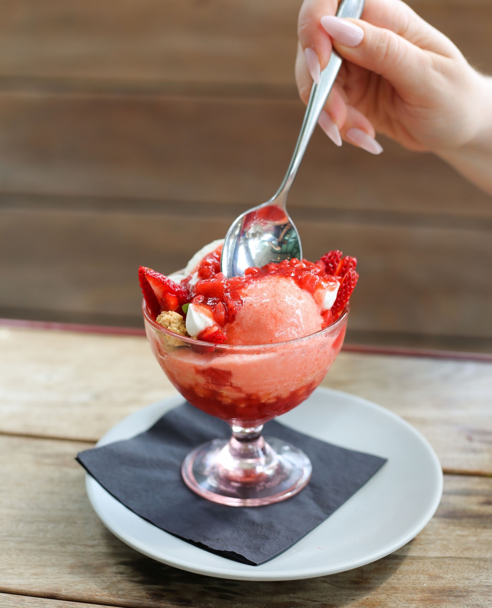 Hand scooping strawberry dessert from a glass on a wooden table.
