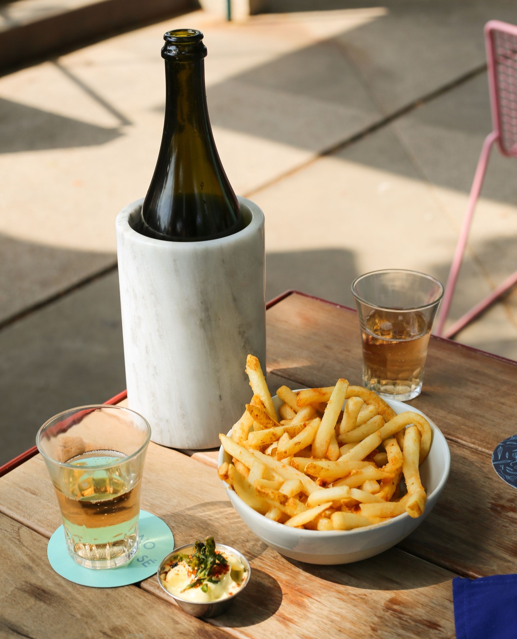Bottle in marble cooler, fries, and two drinks on wooden table.
