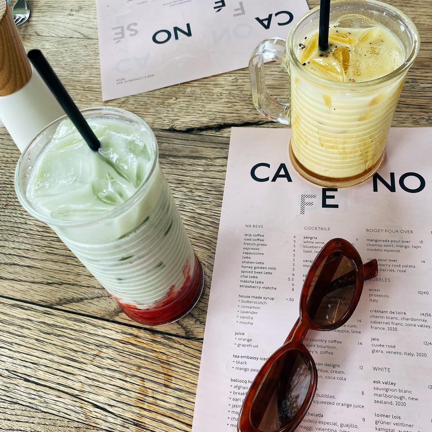 Two iced drinks, menu, and sunglasses on a wooden table.