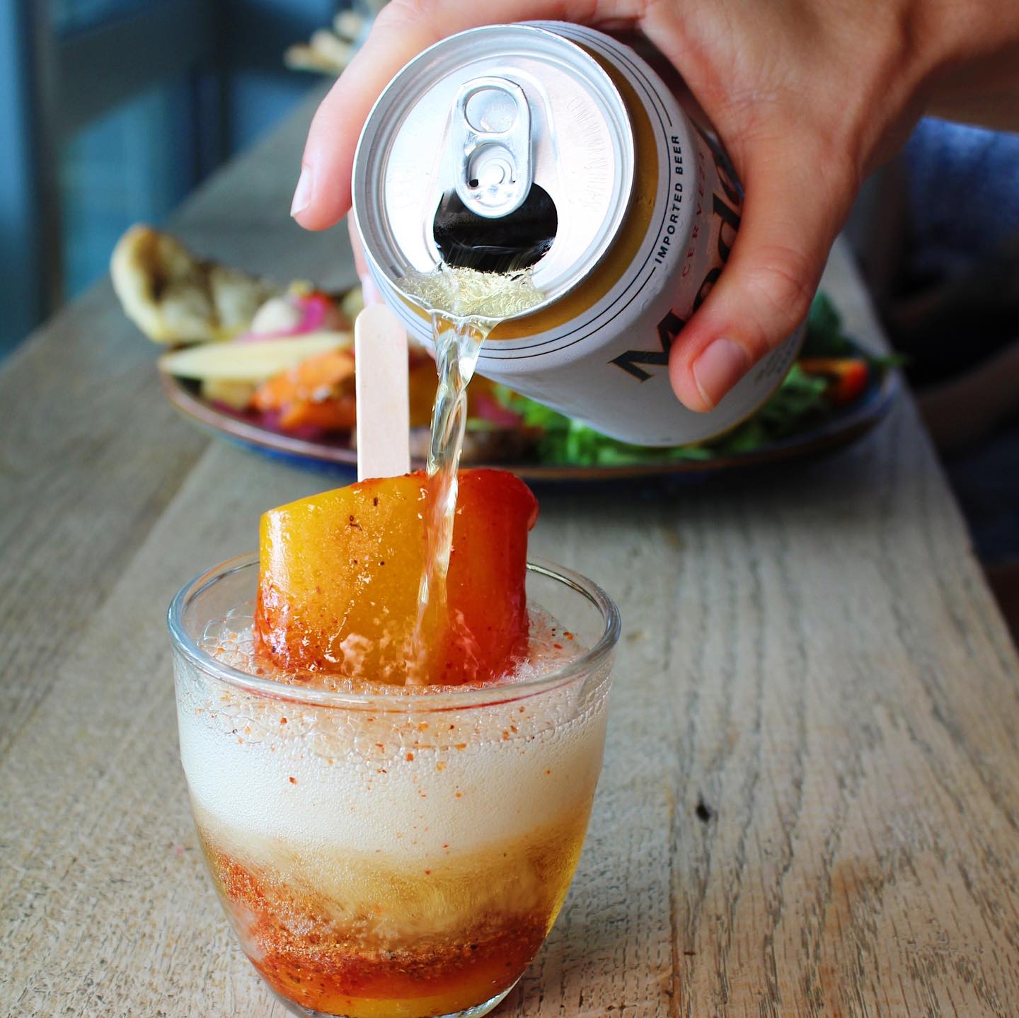 Hand pouring beer from a can into a glass with a fruit popsicle.