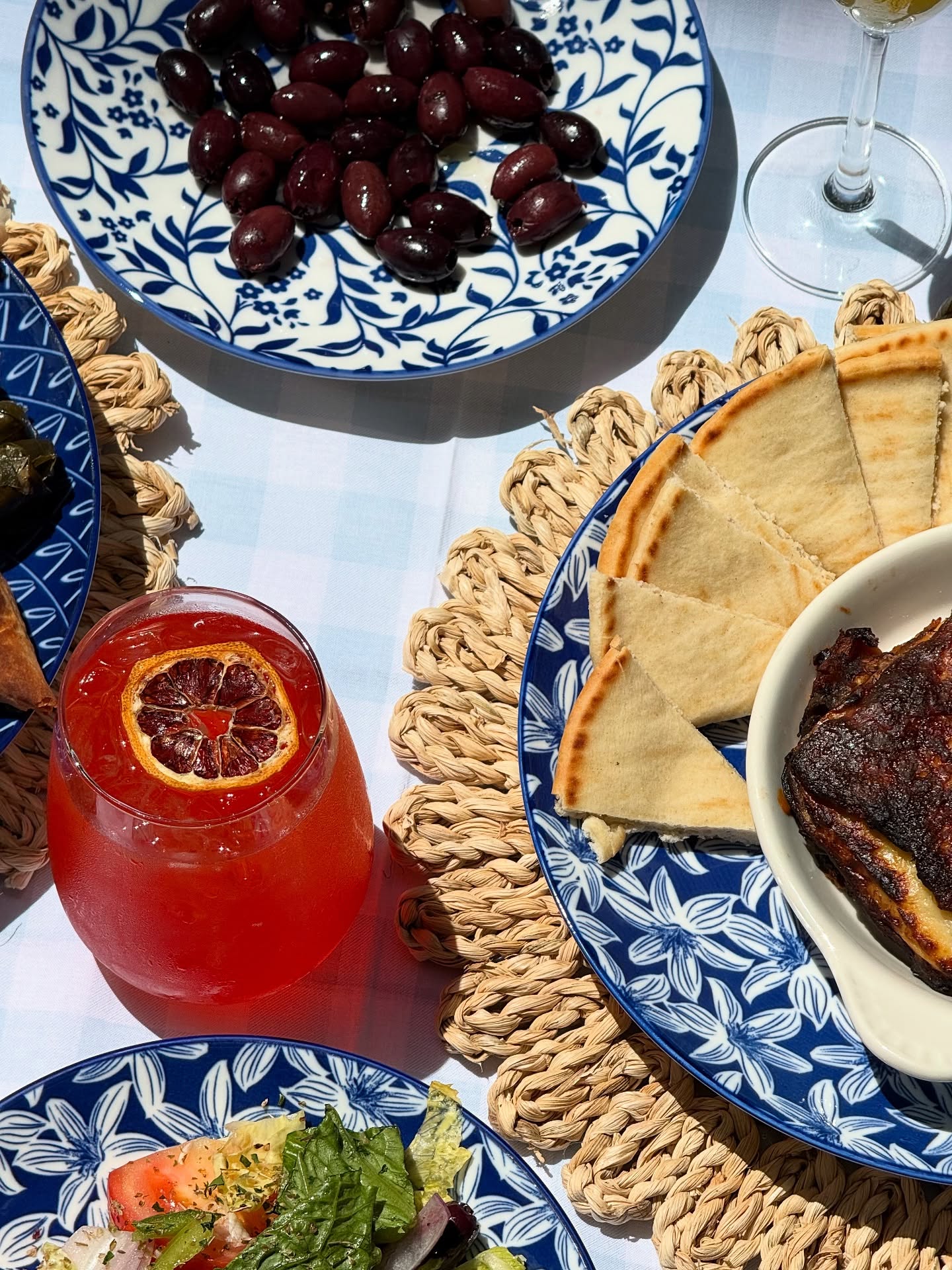 A table set with Greek food, olives, pita bread, and a drink.