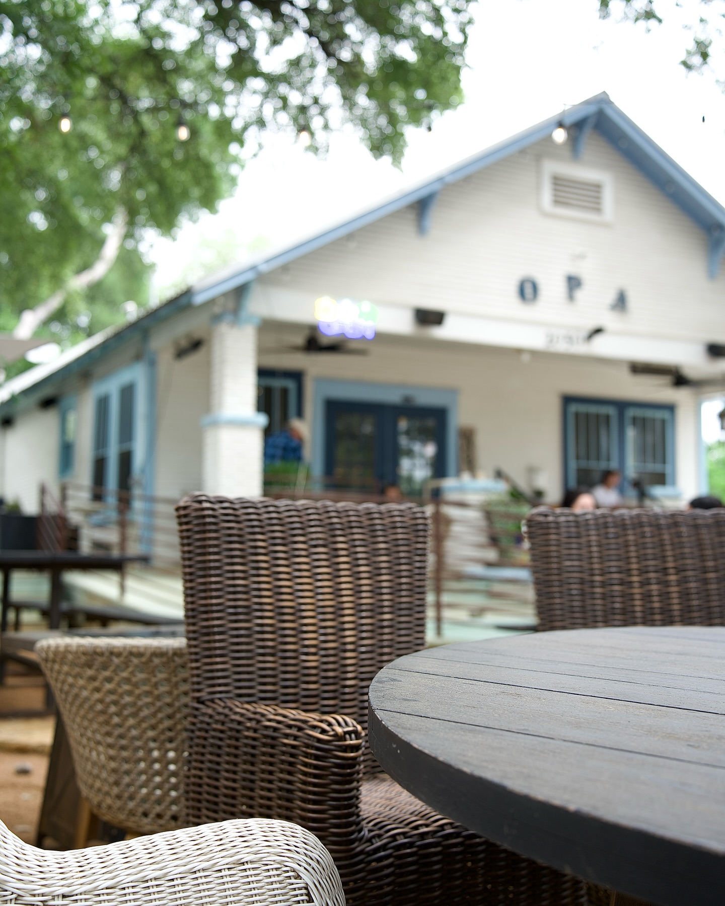Outdoor patio with dark wooden table, wicker chairs, and OPA building.