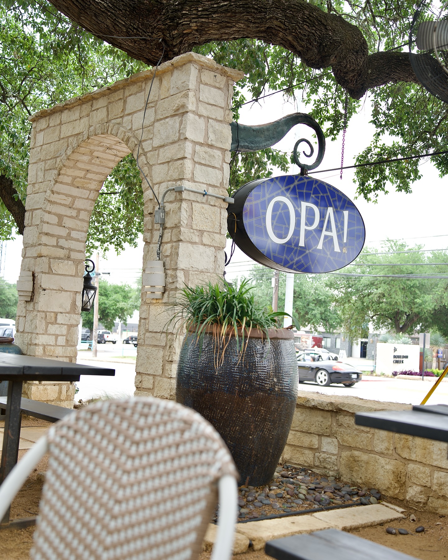 Outdoor stone archway with "OPA!" sign and seating area.