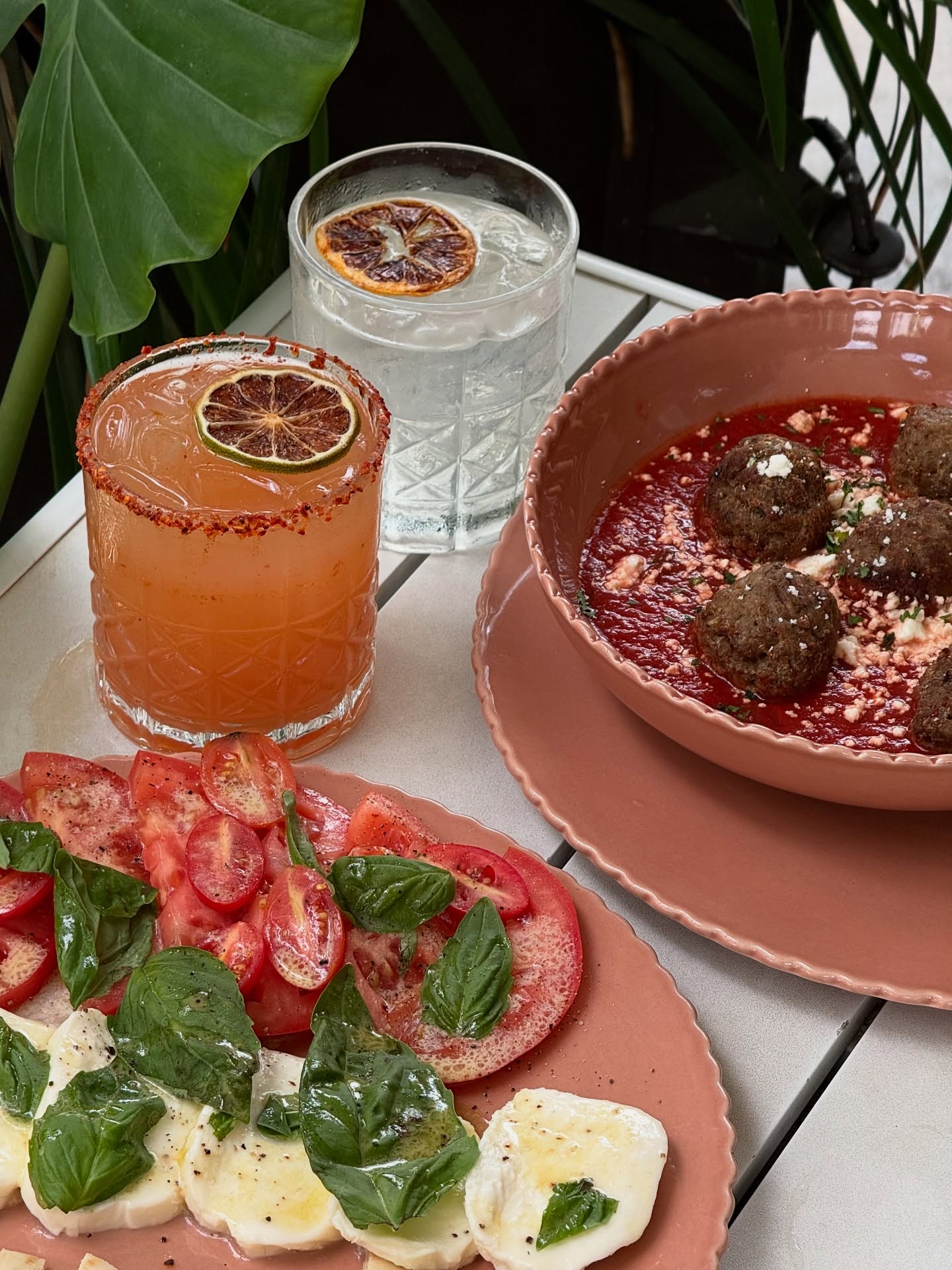 Cocktails, meatballs, and Caprese salad served on a white table.