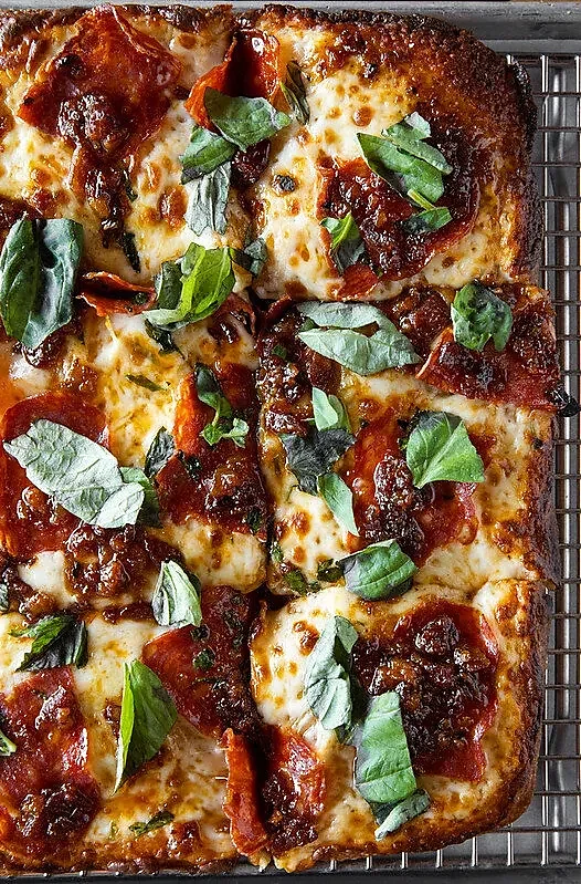 Square pizza with pepperoni, melted cheese and fresh basil on rack