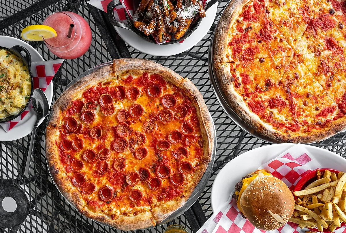 Table spread of pepperoni and cheese pizzas, burger, fries, frozen drink
