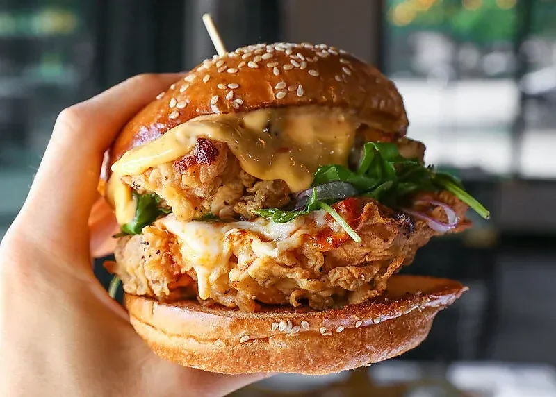 Fried chicken sandwich with melted cheese and arugula on sesame bun