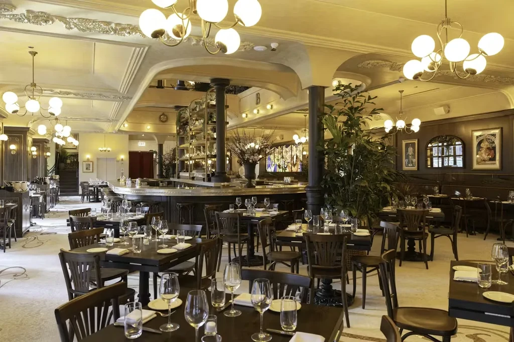 Elegant, empty restaurant with set tables, large bar, and chandeliers.