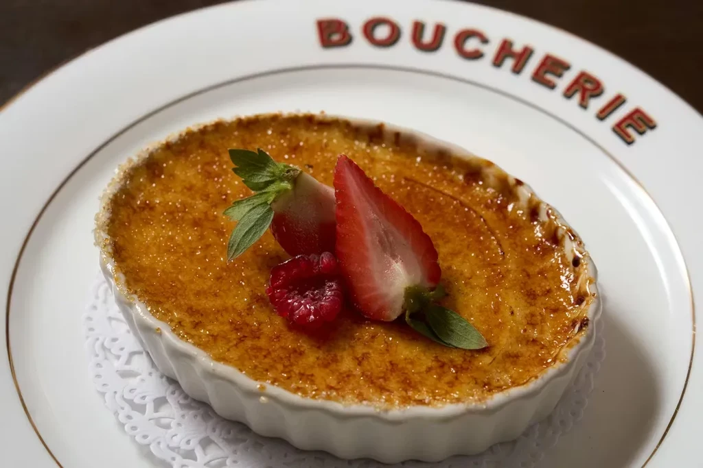 Crème brûlée in ramekin with fruit, on a plate with text.