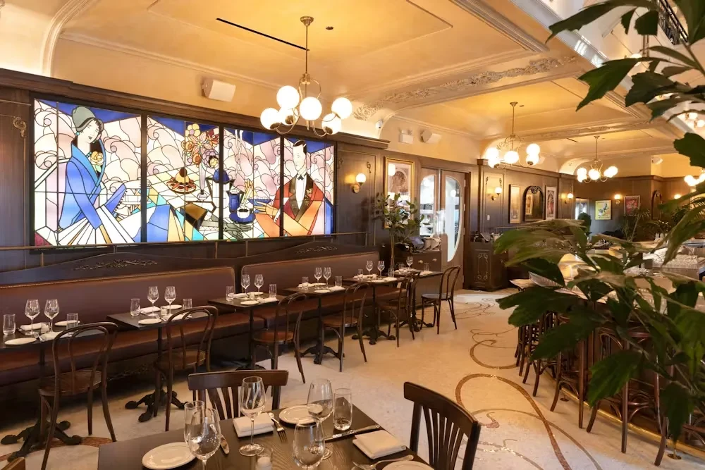 Restaurant interior with booth seating, set tables, and stained-glass art.