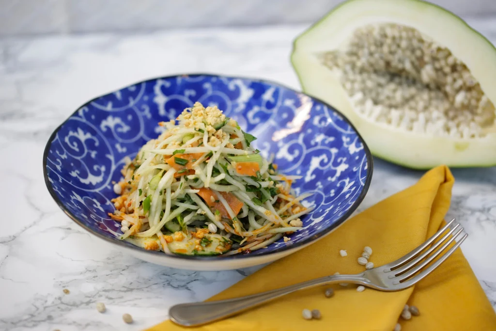 Green papaya salad in a blue and white bowl.