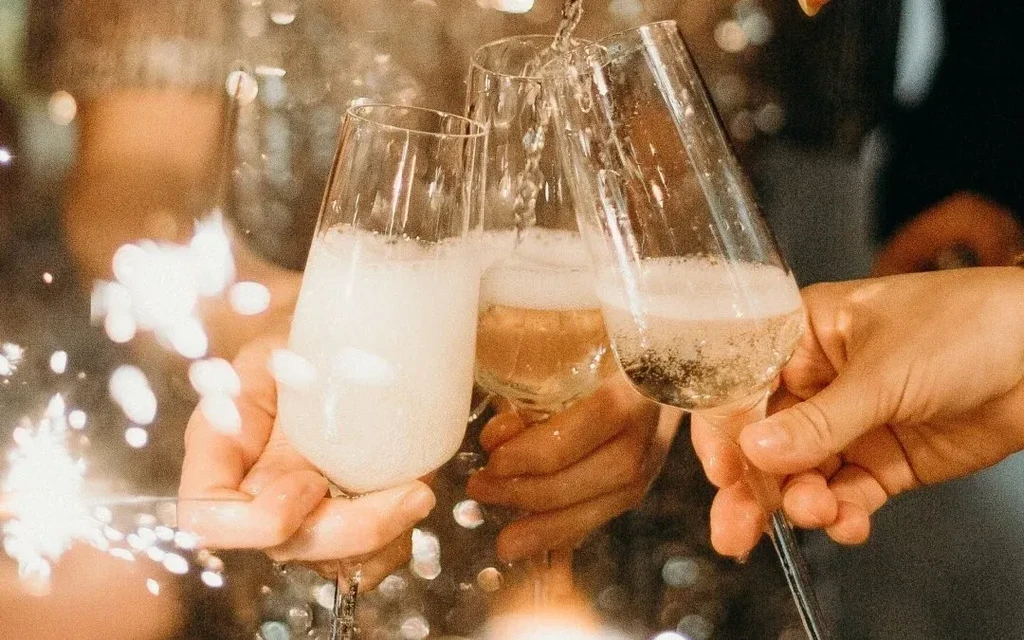 Three hands toast with champagne flutes and a sparkling drink.