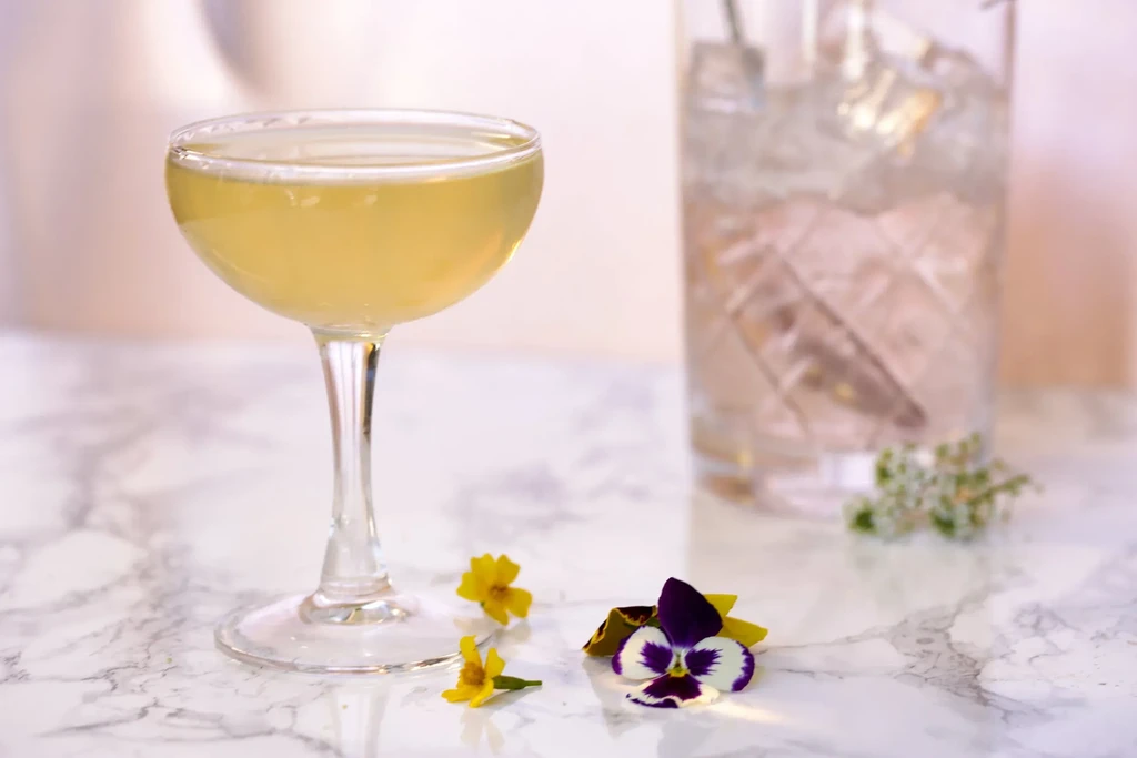 Pale yellow cocktail in a coupe glass with scattered flowers.