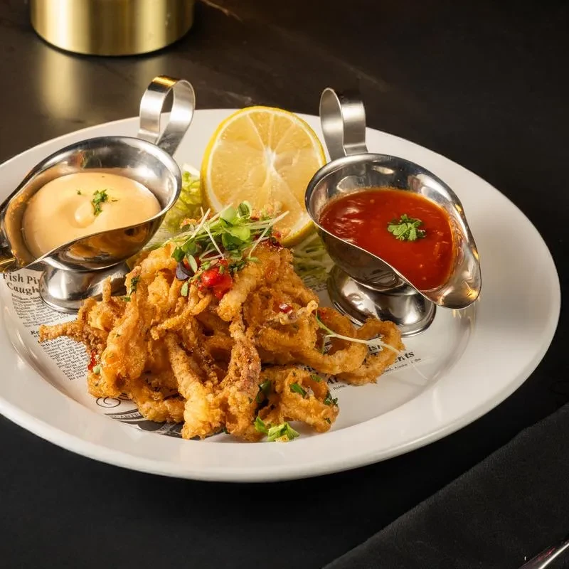 Plate of crispy fried calamari with two dipping sauces and a lemon wedge.