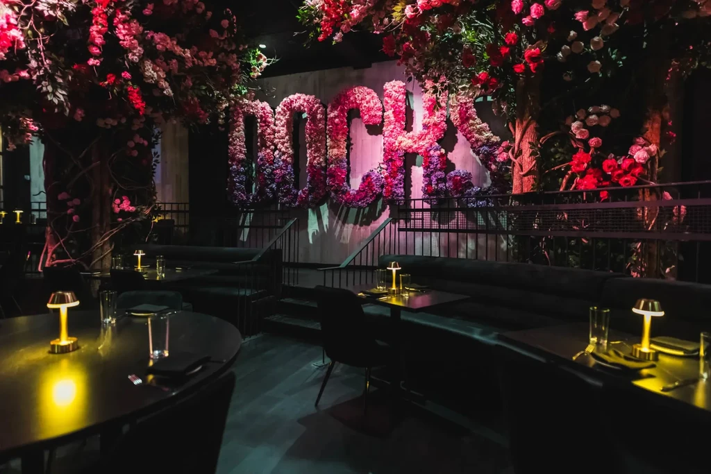 Dark restaurant interior with flower arrangements spelling "MOCH".