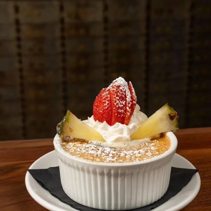 Creme brûlée with whipped cream, strawberries, and pineapple in a ramekin.