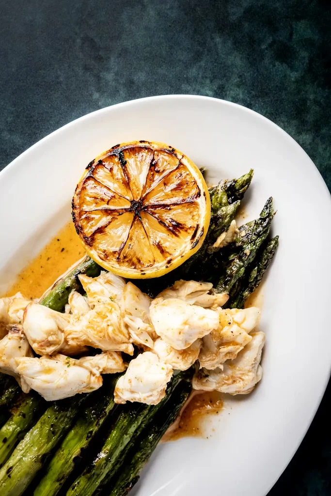 Close-up of a white plate with crab meat, asparagus, and grilled lemon.