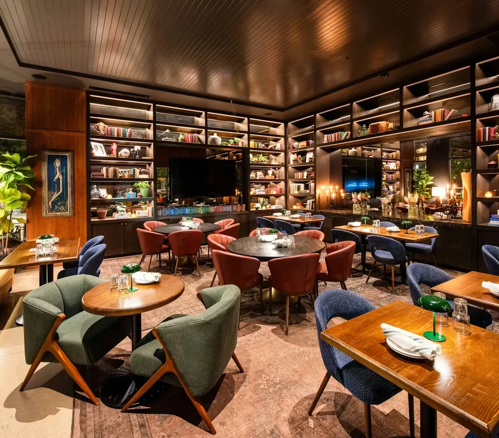 Restaurant interior with set tables, chairs, bookshelves, and ambient lighting.
