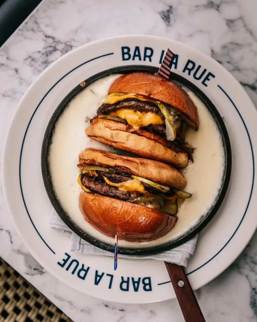 Two double-patty burgers with cheese and pickles in a skillet.