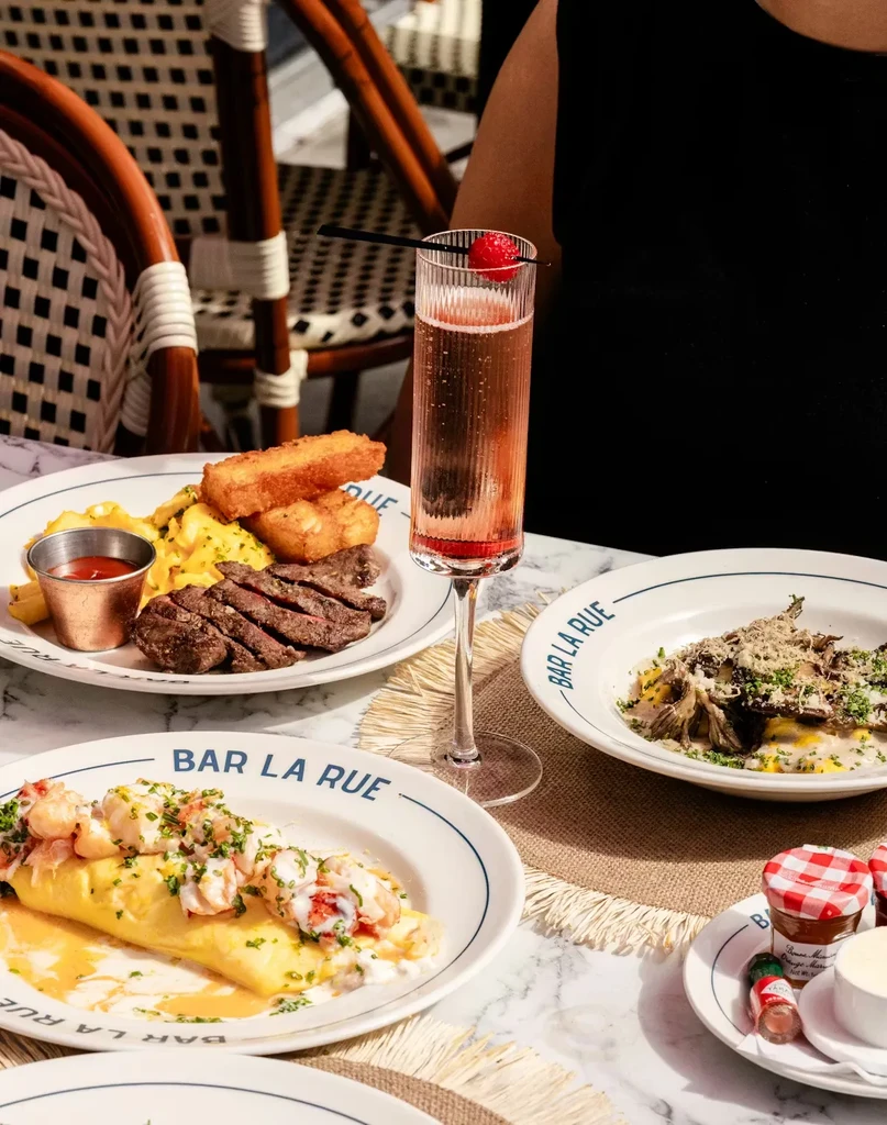 Restaurant table with omelet, steak, scrambled eggs, and a pink drink.
