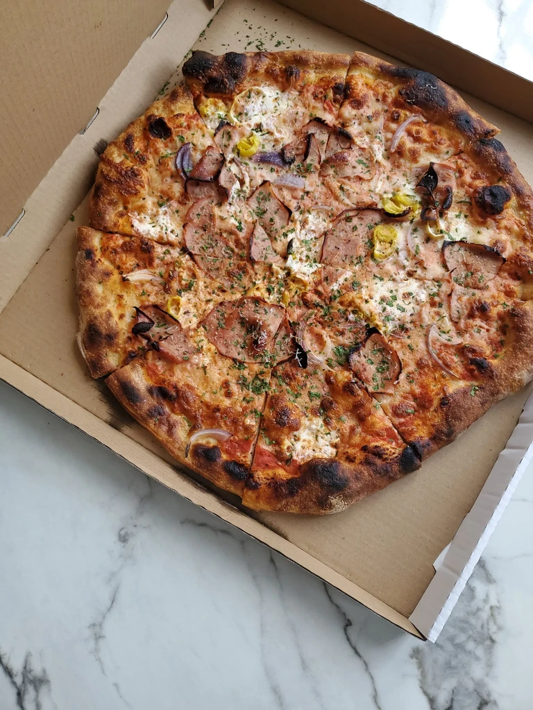 A large, sliced pizza with red onion and pork in a cardboard box.