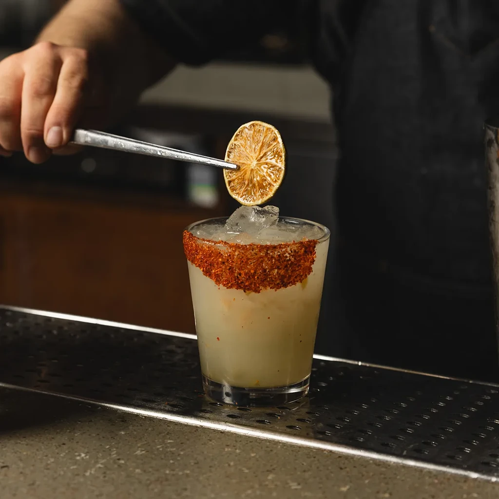 A bartender garnishes a chili-rimmed cocktail with a dried lime slice.