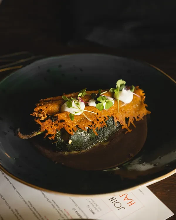 Dark plate with chili relleno in sauce and topped with microgreens.