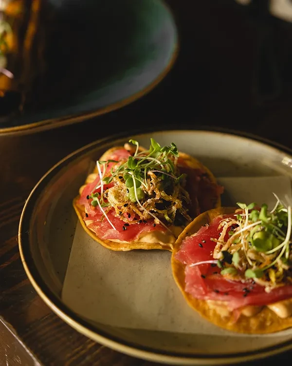 Two tuna tostadas with microgreens and crispy onions on a plate.