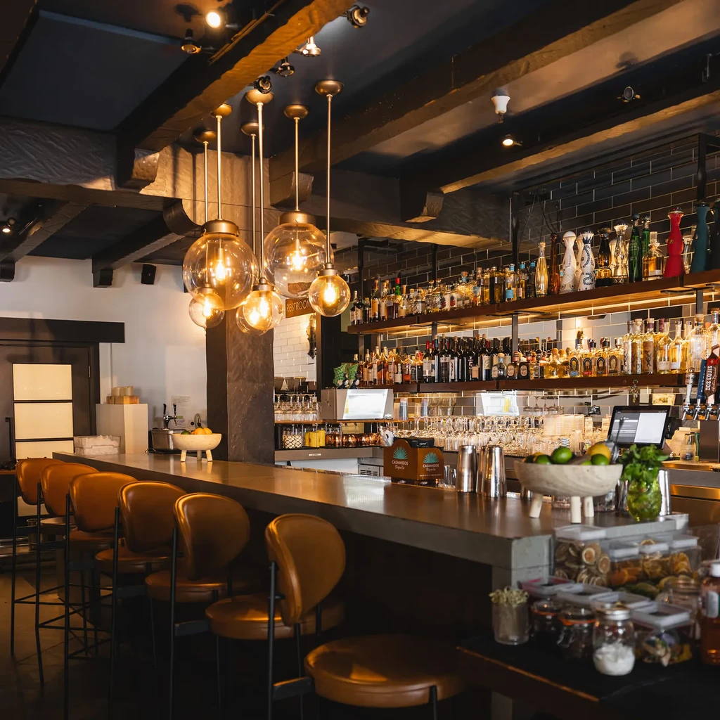 An empty bar with brown stools and shelves of liquor bottles.