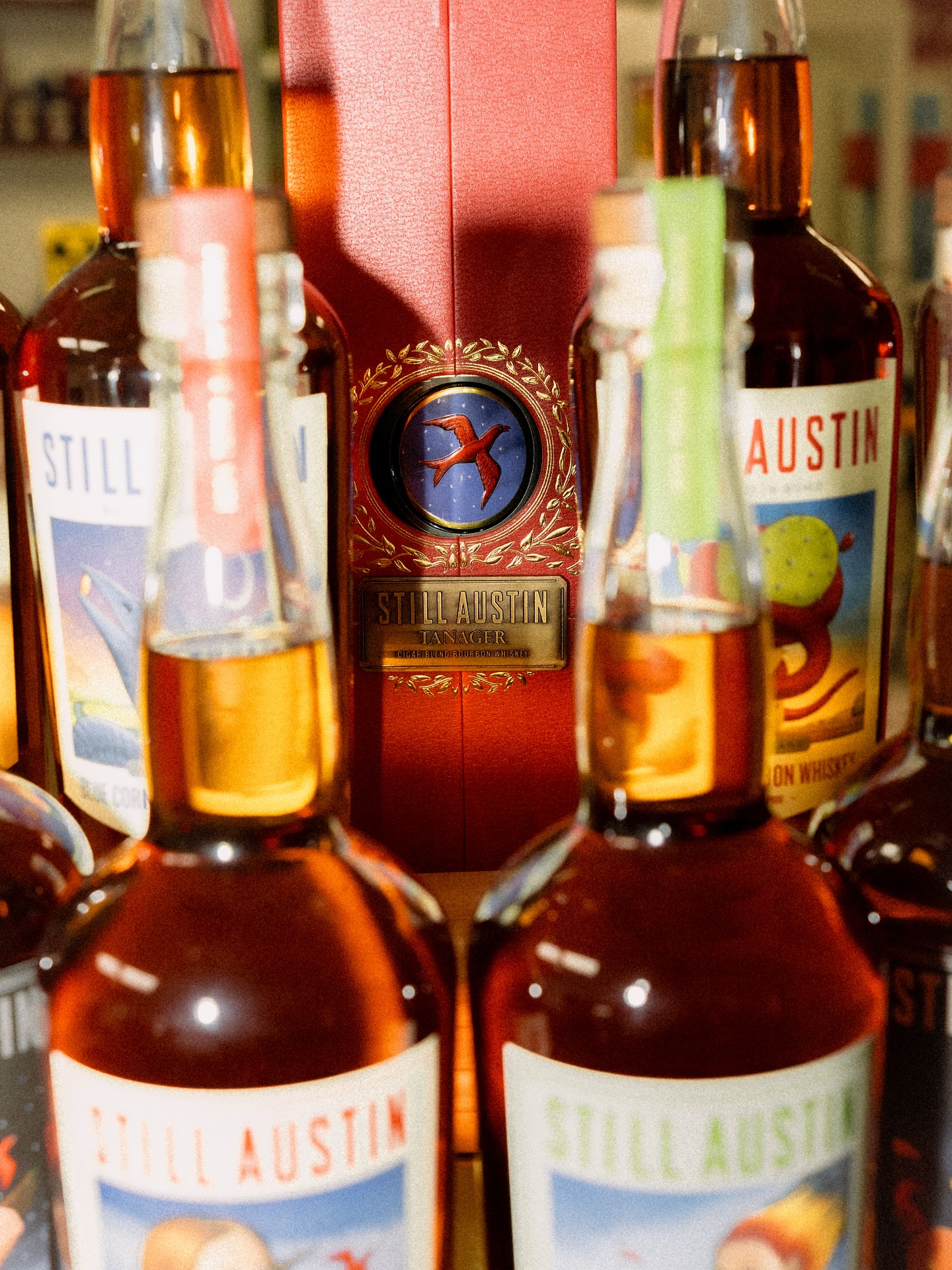 Still Austin whiskey bottles surrounding a prominent red brand box.