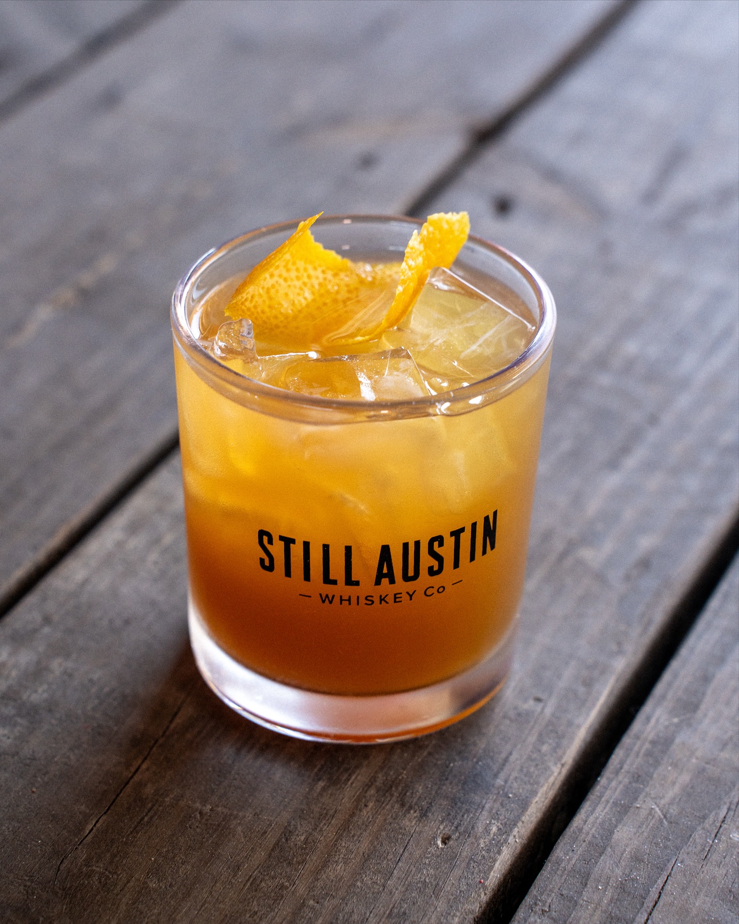Still Austin Whiskey Co. cocktail with orange peel on a wooden table.