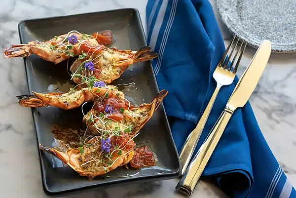 Grilled head-on shrimp with herbs on black rectangular plate