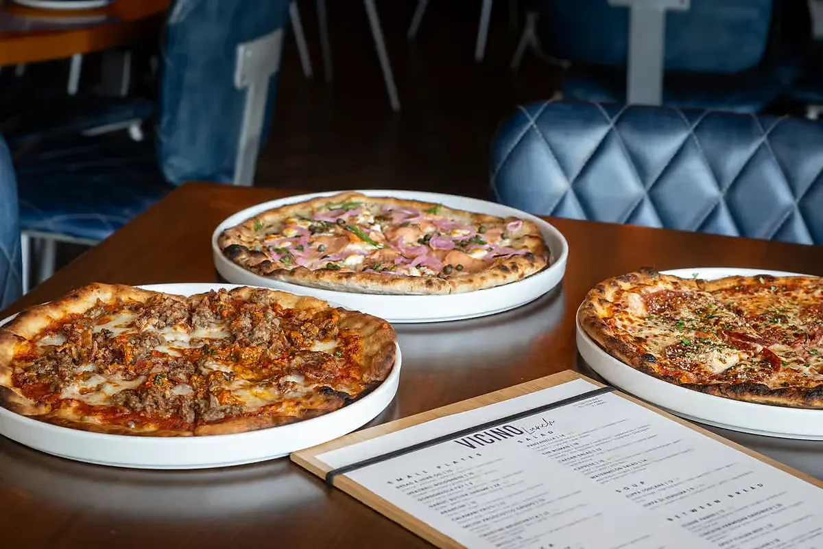 Three thin-crust pizzas on white plates beside a printed menu