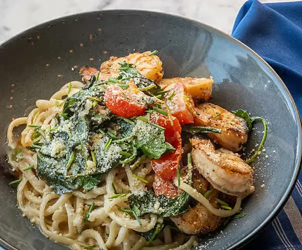 Shrimp pasta with spinach, tomatoes and grated cheese in bowl