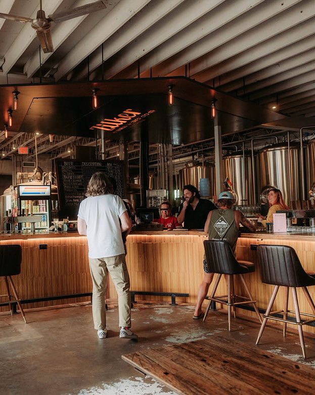 View of a brewery bar with patrons and large fermenting tanks.