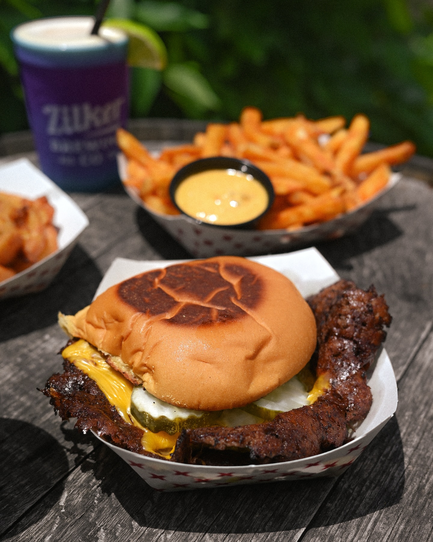 A cheeseburger, fries, and purple drink on a wooden table.