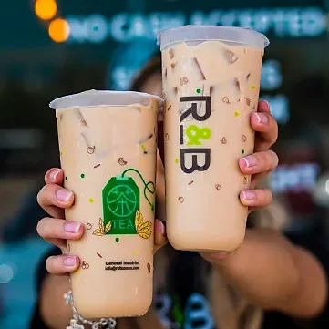 Two hands holding large iced milk teas in branded cups